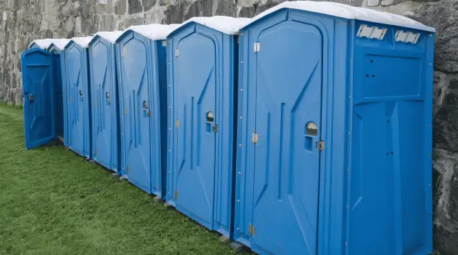 Row of blue portable toilets lined up on grass against a stone wall for event sanitation in Milwaukee, WI