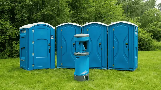 Four blue portable toilets and a matching hand washing station on grass near trees, a common sight at local outdoor events in Milwaukee, WI