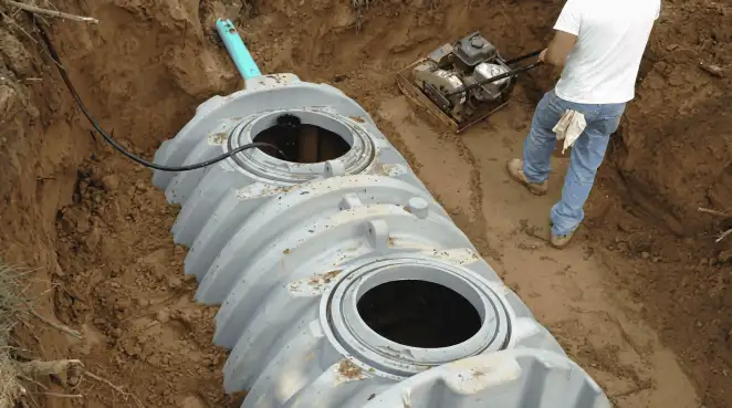 Septic tank installation showing a technician compacting soil around a new poly septic tank in an excavation pit in Milwaukee, WI